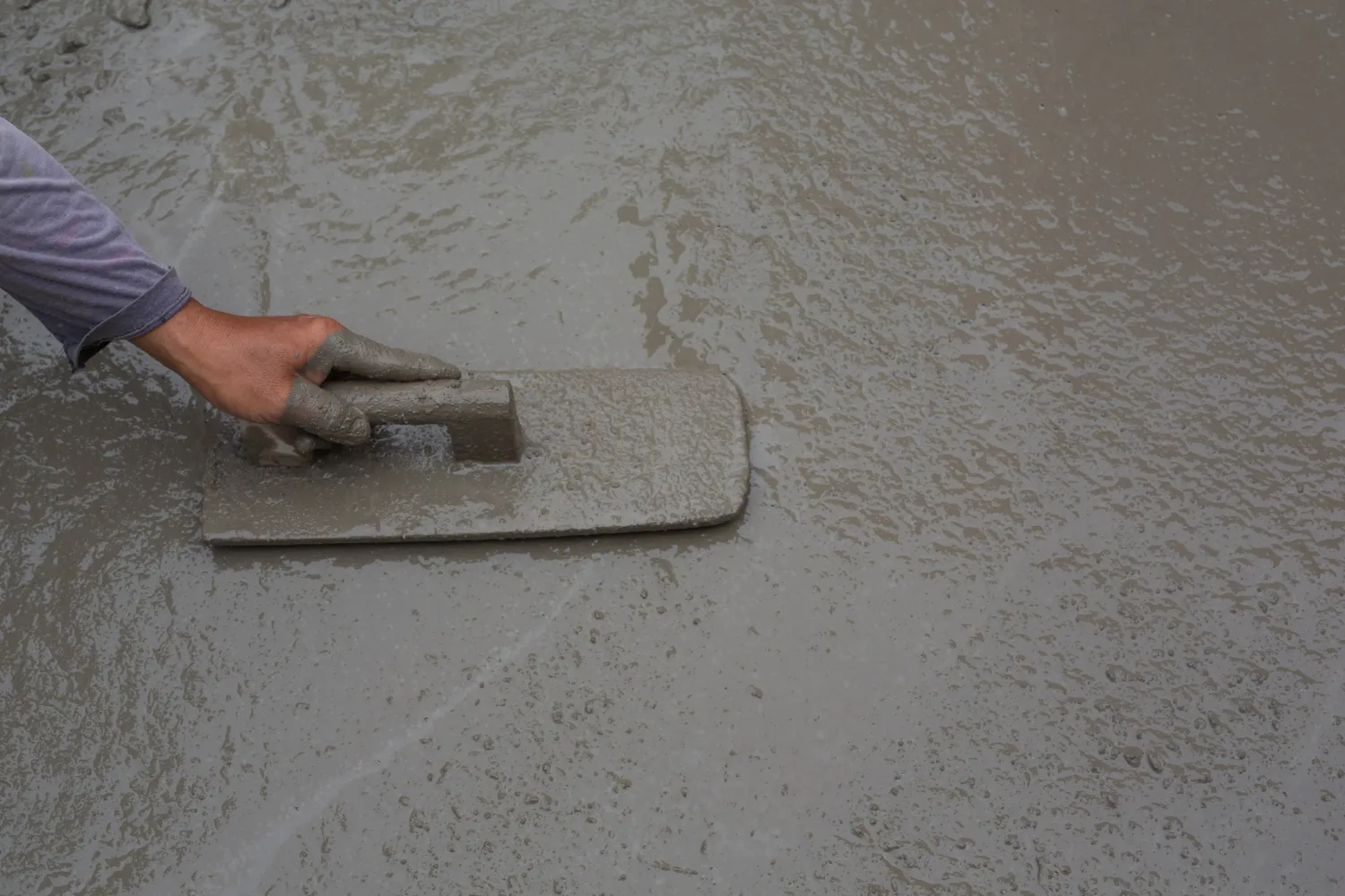 Mano usando una paleta para alisar concreto fresco en una superficie de construcción.